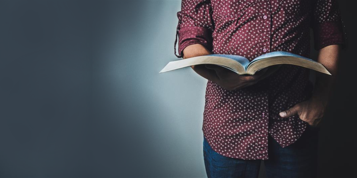 A close-up of a man where it's just his body as he holds the Bible and reads it.