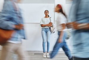 A young woman stands against a wall in distress while people rush by her