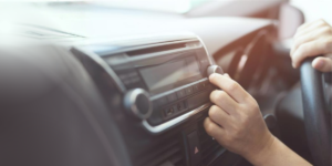 A driver adjusting their car radio. It is a close-up view of the radio with the person's hand twisting the knob.