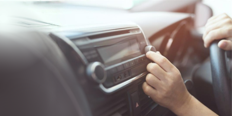 A driver adjusting their car radio. It is a close-up view of the radio with the person's hand twisting the knob.
