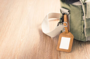 a blank leather luggage tag hanging at the canvas shoulder bag on space of wood floor