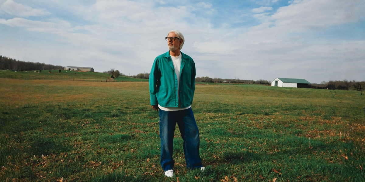 Matt Maher in an open field. Distant farm buildings are behind him.