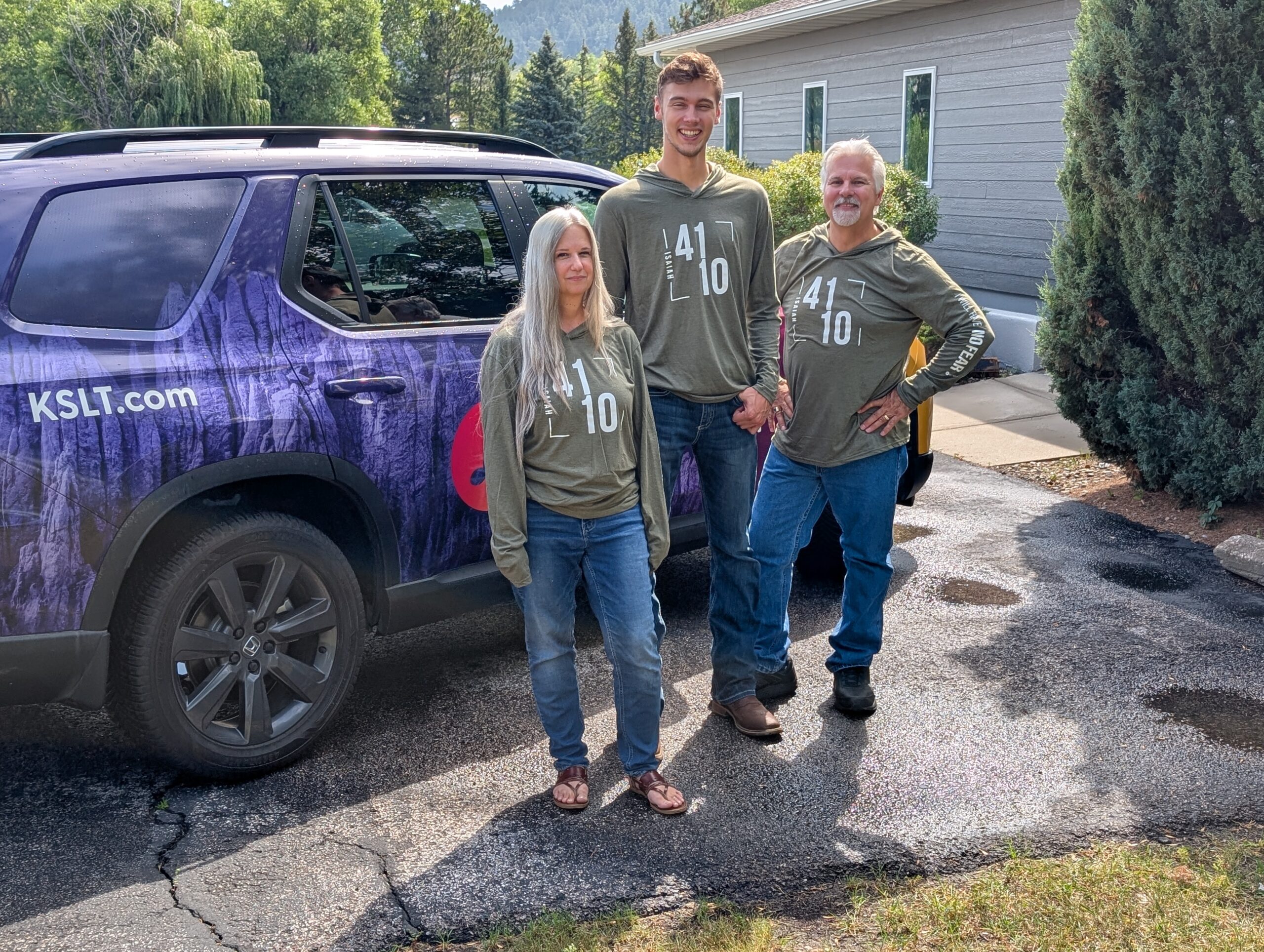 KSLT staff wearing Team 40 shirts and standing in front of car
